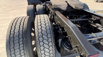 Truck chassis showing dual rear axles and tires with heavy-duty suspension; components of the frame and air tanks visible.