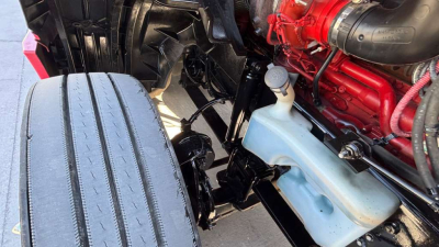 Truck engine bay and front wheel area showing coolant reservoir and diesel engine components.