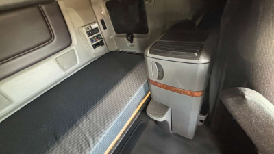 Truck cab interior showing sleeper berth with grey mattress, control panel, and storage unit with wood trim in a cab.