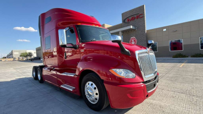 International LT625 sleeper tractor with glossy red paint showing front grille, headlights, and side mirrors. Cab features chrome bumper and step rails; background includes dealership building.