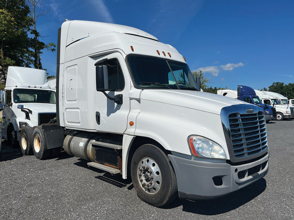 White Freightliner Cascadia125 tractor cab in a used truck lot, with a chrome grille, large windshield, and side mirrors. See the text on stock and VIN placards in the listing context.