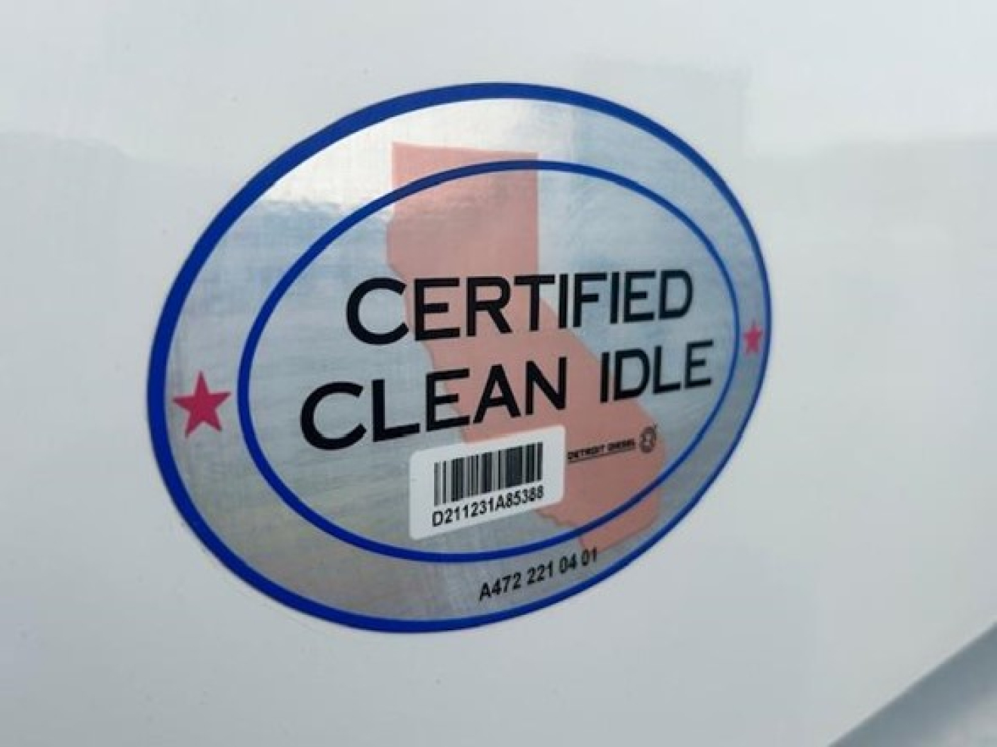 Truck side sticker reading 'CERTIFIED CLEAN IDLE' with a barcode underneath; circular blue and pink logo on a white surface.