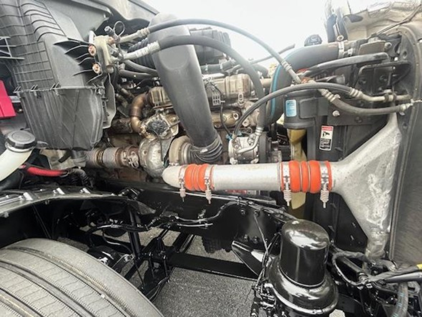 Truck engine bay showing diesel engine components, hoses, and radiator area of a Freightliner Cascadia 126 with visible piping and reservoirs.