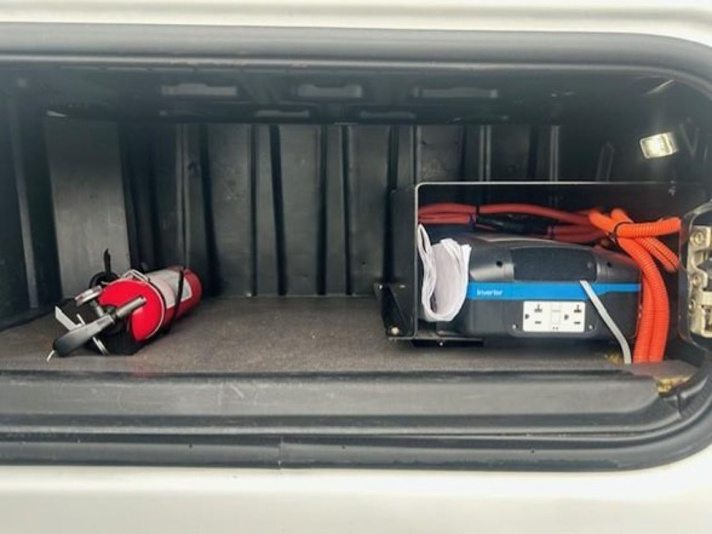 Truck storage compartment showing a portable power inverter and a red fire extinguisher in the rear pocket of a Freightliner Cascadia cab.