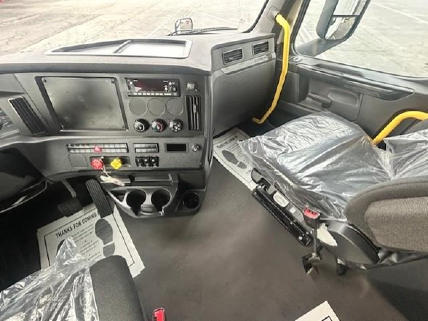 Cab interior of a Freightliner Cascadia 126 truck showing dashboard with radio, climate controls, cup holders, and driver's seat.
