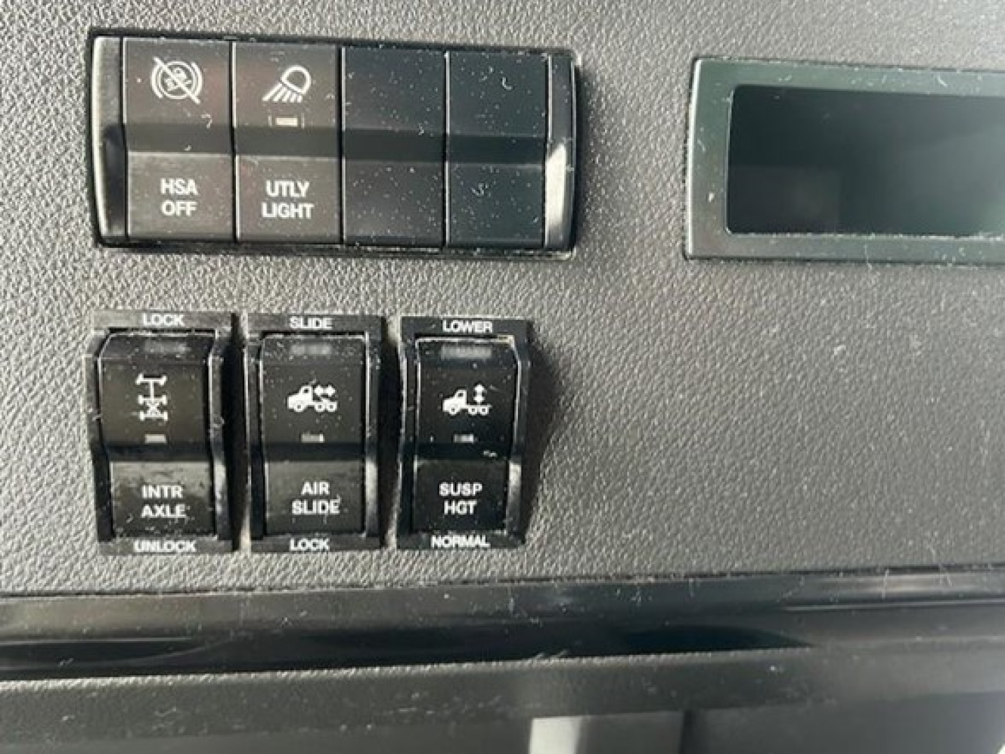 Dashboard switches and controls in a Freightliner Cascadia cab showing HSA off, UTY light, intr axle/air suspension controls, and lower window/lock switches.