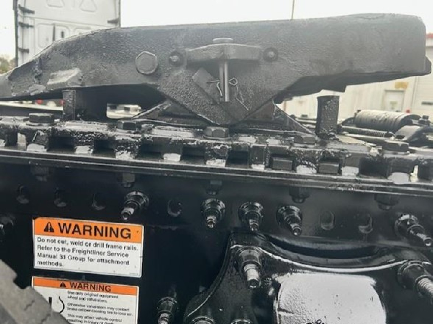 Truck engine bay area with warning labels and drill-lattice mounts visible; warning labels contain text "WARNING Do not enter..." around fluids; black metal components with bolts.