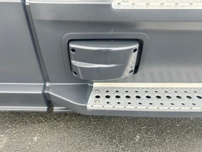 Truck entry step and door area of a Freightliner Cascadia 126 cab with a foldable step, close-up of side door handle and textured metal running board.