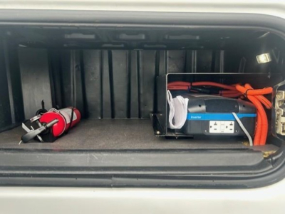 Truck storage compartment showing a portable power inverter and a red fire extinguisher in the rear pocket of a Freightliner Cascadia cab.