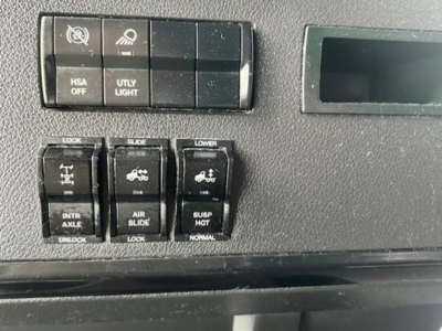 Dashboard switches and controls in a Freightliner Cascadia cab showing HSA off, UTY light, intr axle/air suspension controls, and lower window/lock switches.