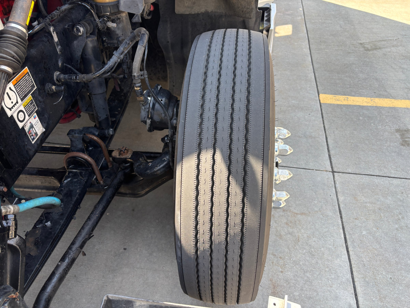 Front wheel and suspension area of a 2023 Kenworth T680 sleeper truck showing dual rear tires and framework, with visible tire tread and nearby components.