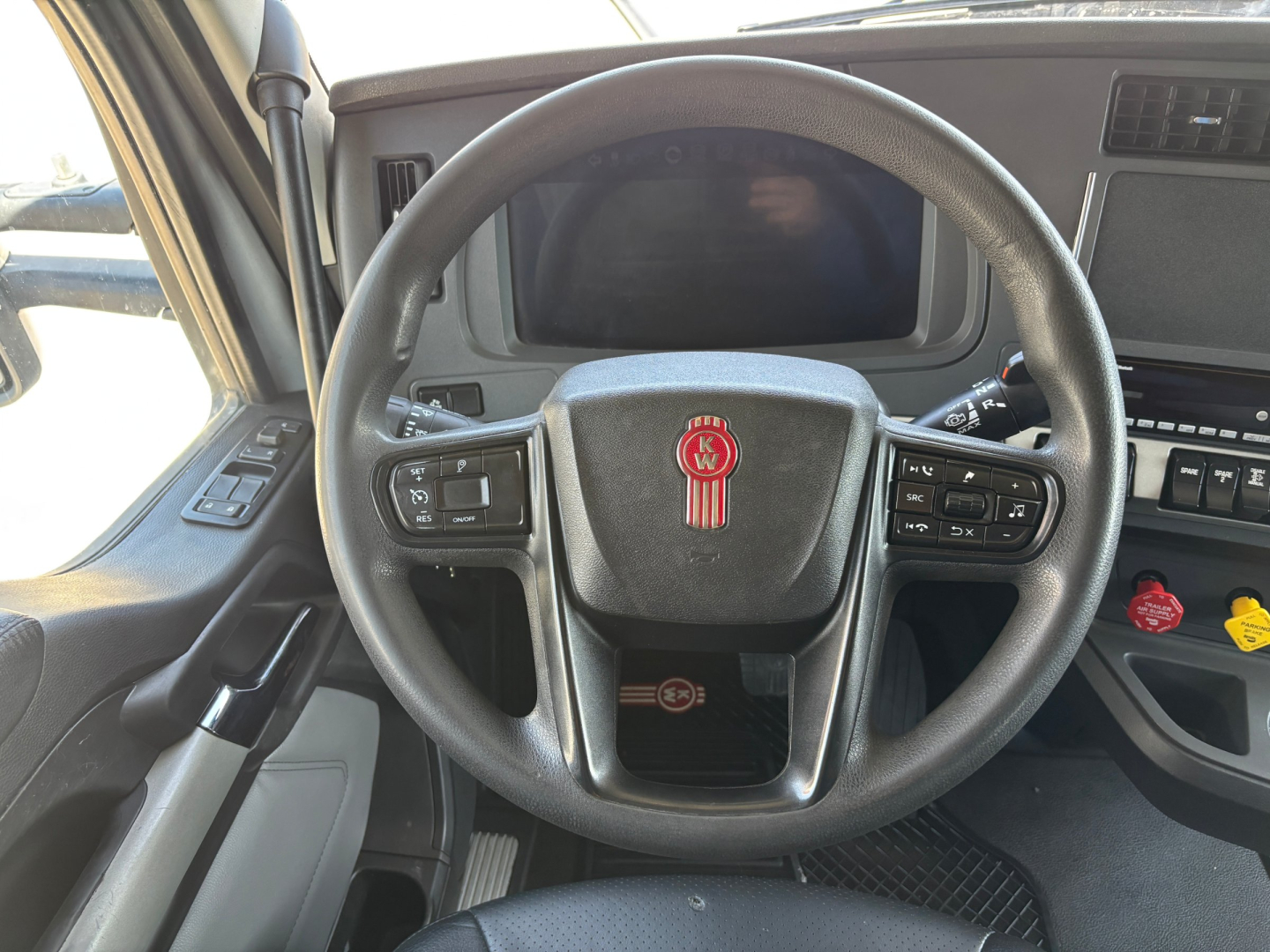 Kenworth T680 interior showing steering wheel with KW emblem, dashboard screen, and control stalks.