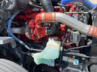 Kenworth T680 engine bay showing coolant reservoir and turbocharger with red engine components and orange intake tube.