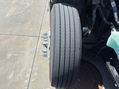 Truck front wheel and brake assembly showing wheel and lug nuts; portion of engine bay and reservoir visible.