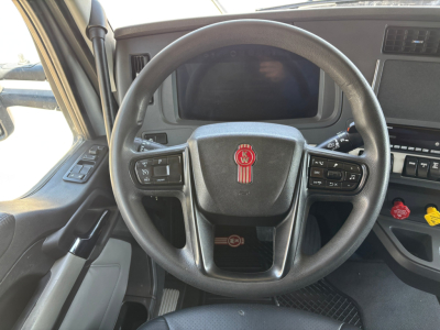 Kenworth T680 interior showing steering wheel with KW emblem, dashboard screen, and control stalks.