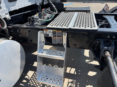 Kenworth T680 chassis area showing perforated aluminum steps and mounting platform with warning labels and hydraulic lines.