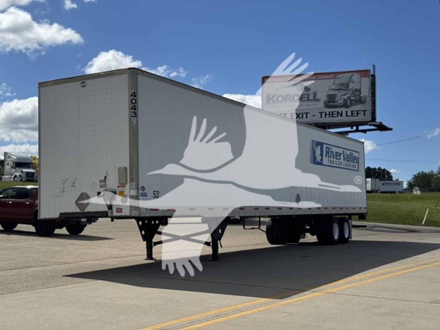 Trailer side-view showing a white utility van trailer with 4043-1 vertical number, parked on road near billboard.