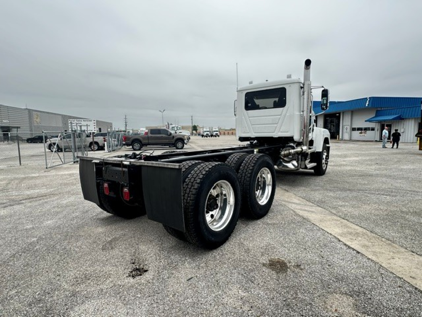 Truck chassis with dual rear axles and cab in the distance; rear view shows dual rear tires and hitch area.