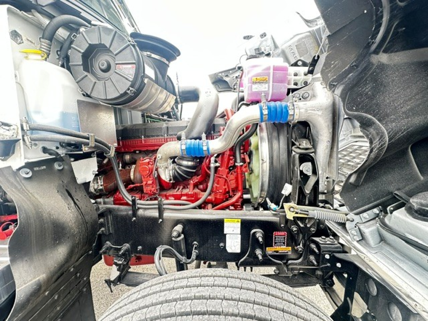 Mack PI64 engine bay showing diesel engine with red engine block, hoses, radiator, and various reservoirs.
