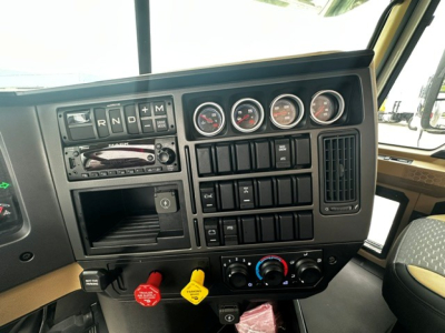 Dashboard of a Mack PI64 cab and chassis showing gear selector, gauges, switches, and climate controls with red and yellow knobs.