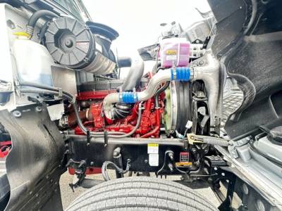Mack PI64 engine bay showing diesel engine with red engine block, hoses, radiator, and various reservoirs.