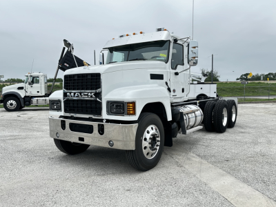 White Mack PI64 cab and chassis truck showing front grille with Mack emblem, chrome bumper, and dual rear axles; side shows fuel tanks and steps.