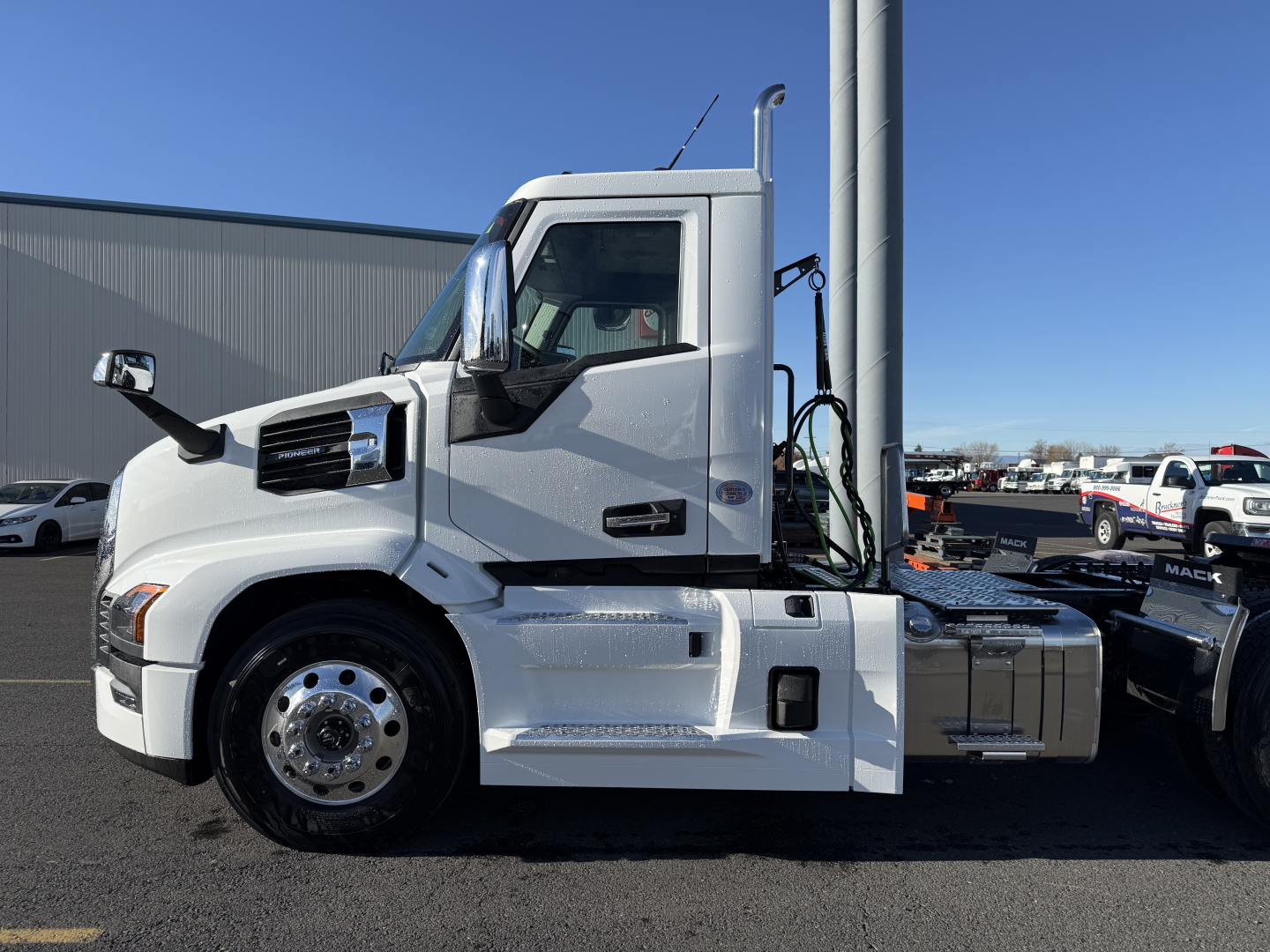 Mack PR64T conventional daycab truck side view showing white cab, chrome fuel tank, and steps.