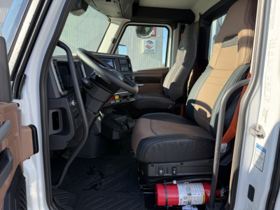 Truck cab interior of a 2026 Mack PR64T showing driver's seat, steering wheel, dashboard, and passenger seat. Some labels and controls visible.