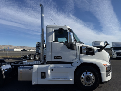 Truck cab side view of a 2026 Mack PR64T with chrome exhaust stack, large front wheel, and side steps; appears in a dealership lot.