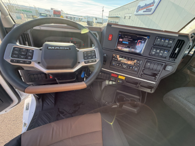 Mack PR64T truck interior showing steering wheel, dashboard, and touchscreen display with controls and gear selector.