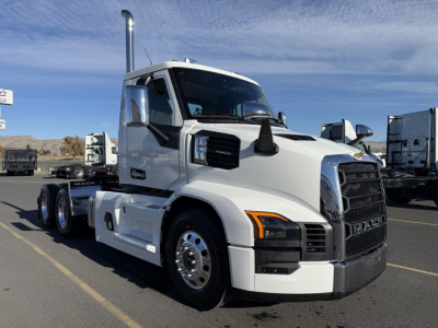 Mack PR64T conventional daycab truck in a parking lot with chrome exhaust stacks, white cab, black grille, and dual rear axles.