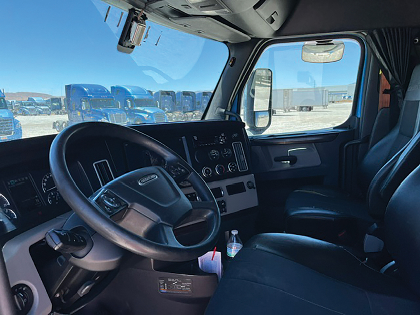 Freightliner Cascadia truck interior driver's seat and dashboard in view with steering wheel, instrument cluster, and center console.