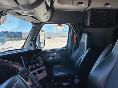 Cab interior of a 2020 Freightliner Cascadia126 sleeper truck showing driver seat, passenger seat, dashboard, steering wheel, and side window with daylight.