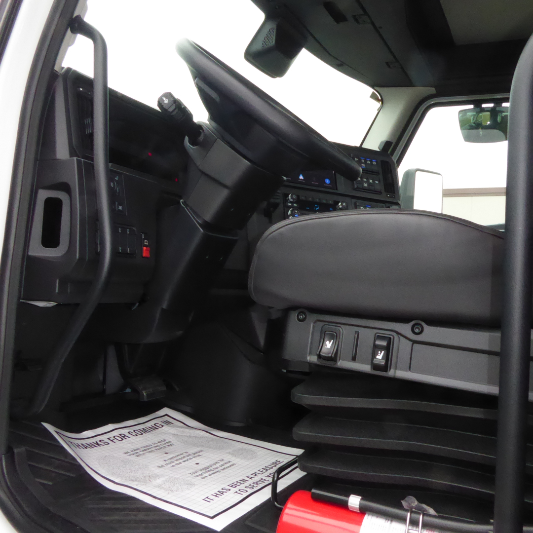 Dashboard and driver seat area of a 2026 Mack PR64T conventional daycab inside cab showing steering wheel and control panels.