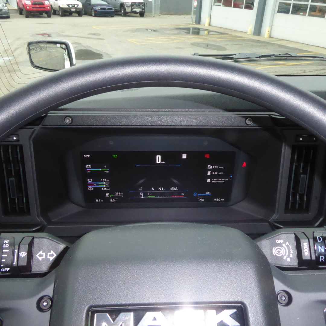 Dashboard view of a 2026 Mack PR64T truck showing digital gauge cluster, steering wheel with Mack logo, and side mirrors.