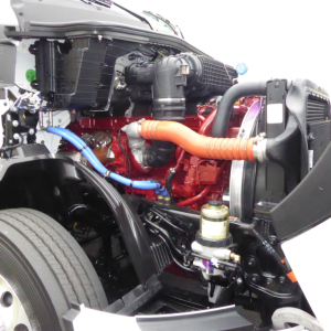 Mack PR64T engine bay showing red engine block, blue and orange hoses, radiator, and brake reservoir.