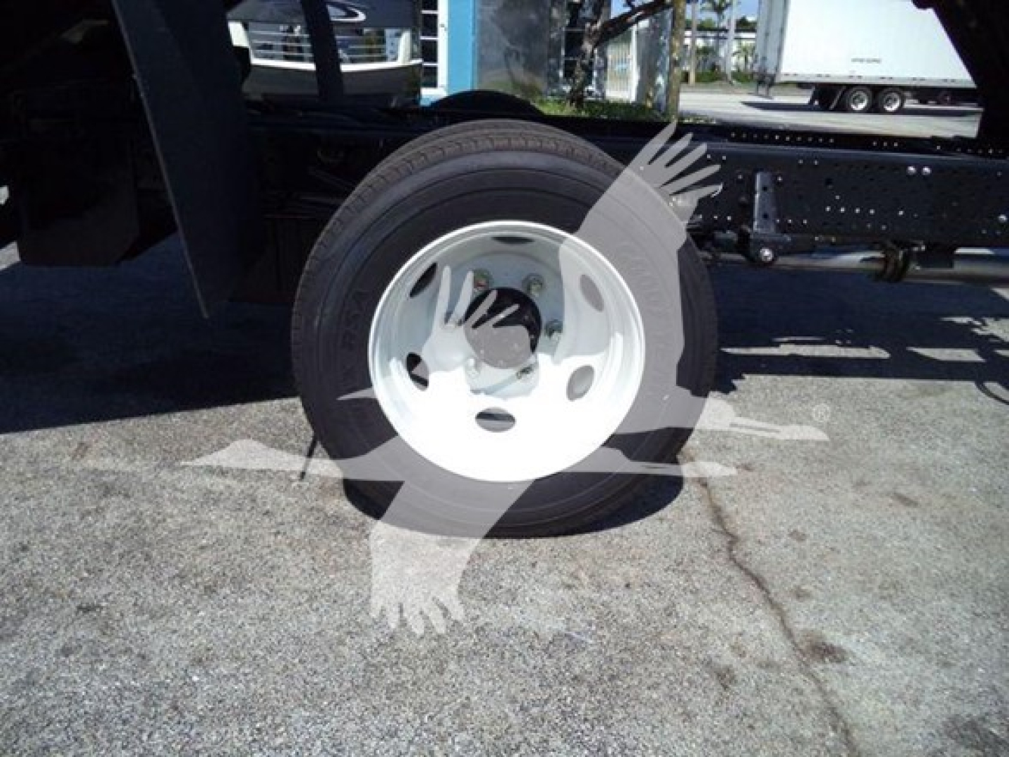 Isuzu NPR HD truck wheel and tire exposed, wheel rim and undercarriage visible, portion of chassis side frame and ground surface