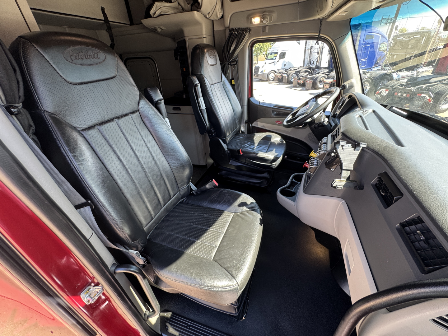Peterbilt 579 truck cab interior showing black leather driver seat and passenger seat with dashboard and steering wheel visible