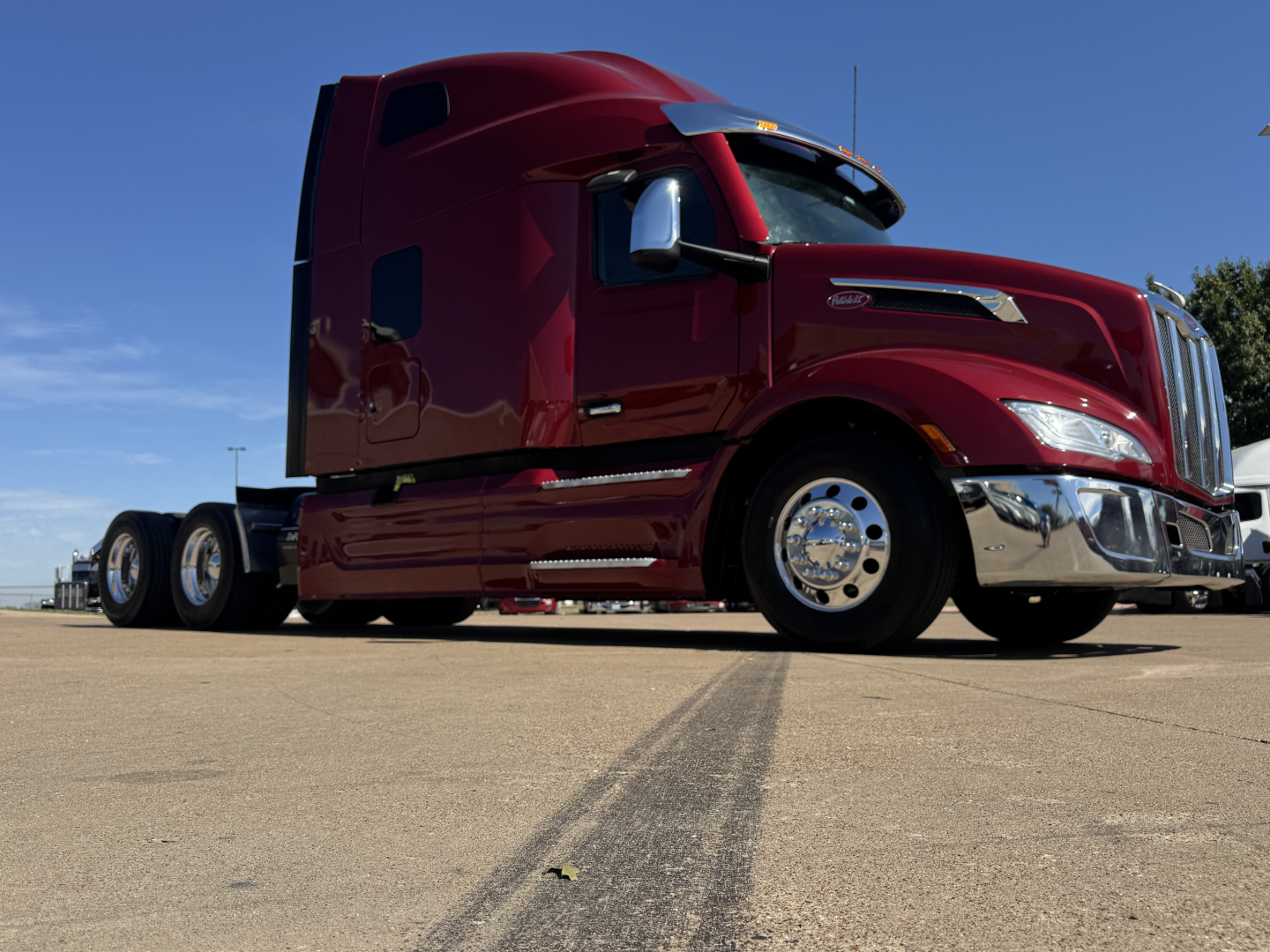 Peterbilt 579 conventional sleeper truck in maroon with chrome accents, side view showing cab, front wheel, and hitch area.