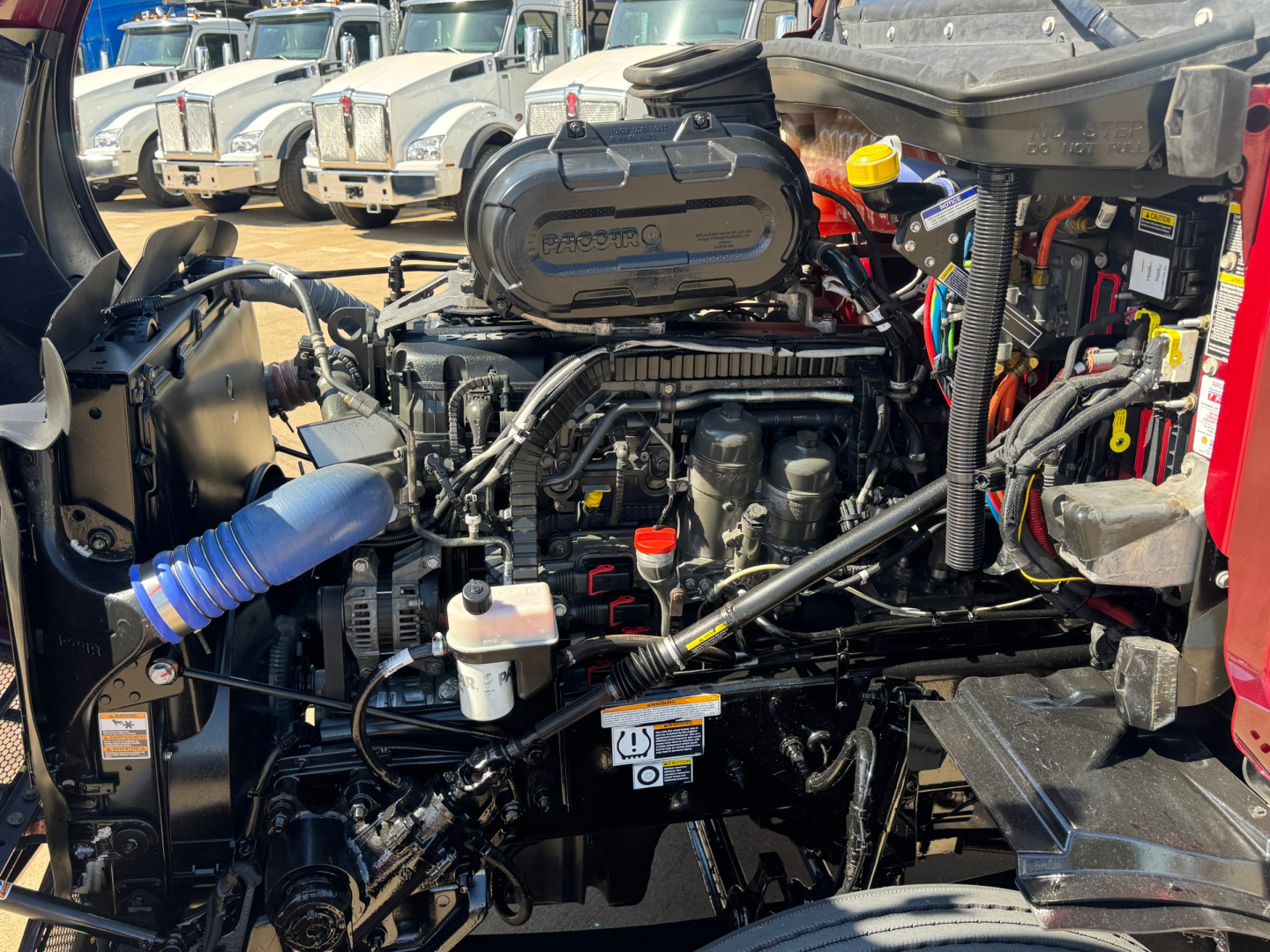 Peterbilt 579 engine bay showing 6-cylinder diesel engine with air intake snorkel and various hoses and reservoirs.