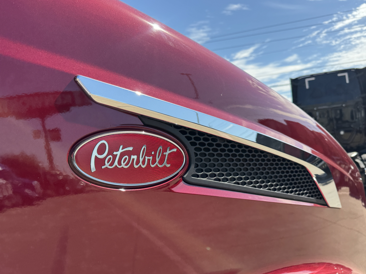 Peterbilt emblem on a red truck hood with grille and chrome accent, close-up view of the Peterbilt badge