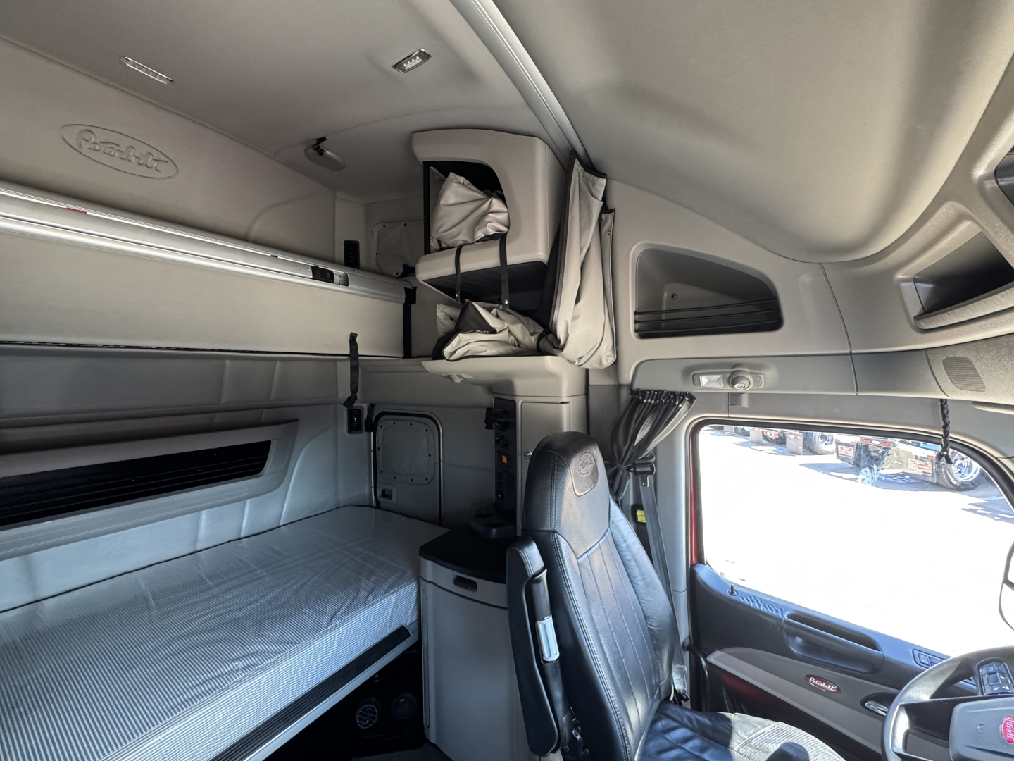 Interior of a Peterbilt 579 sleeper cab with bunk bed, overhead storage, and driver's seat; visible panels and window.