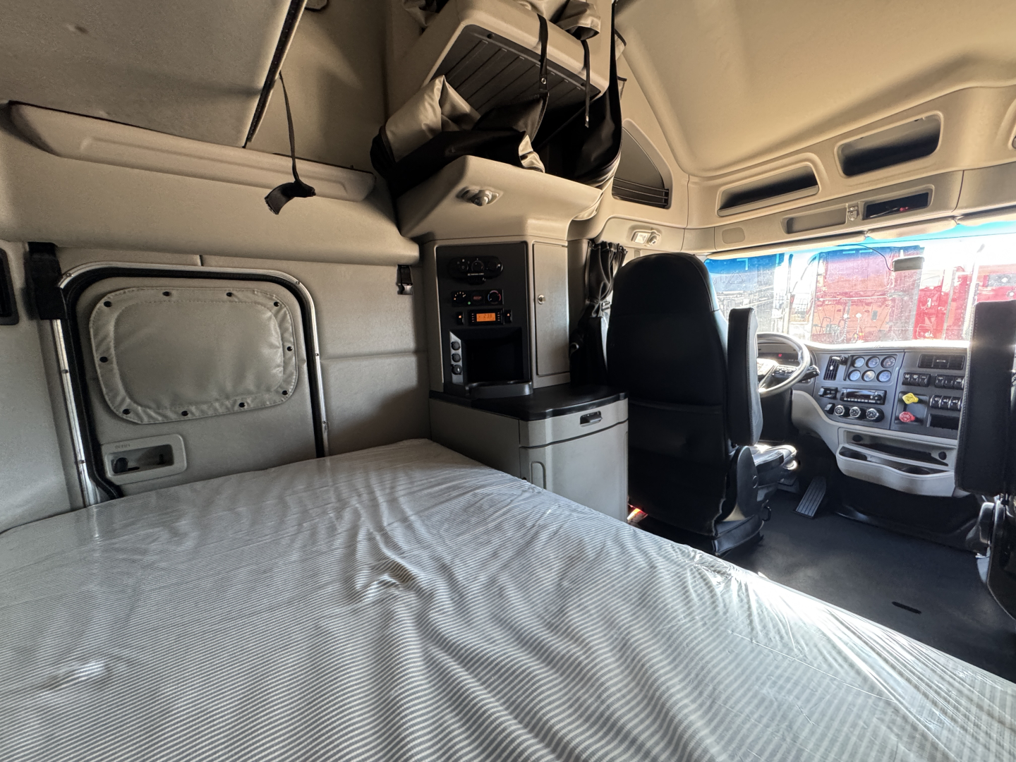 Truck cab interior of a 2023 Peterbilt 579 sleeper showing a bed, overhead storage, and driver seat with dashboard in view.