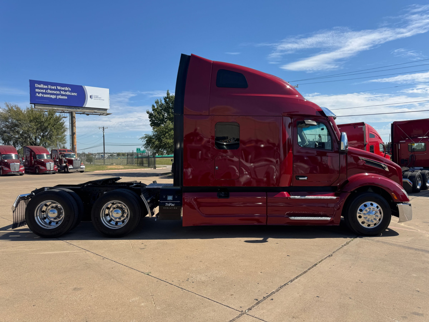 Peterbilt 579 tractor-trailer cab side view showing red exterior, two rear axles, windows, and chrome wheel rims.