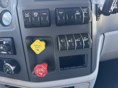 Peterbilt 579 truck dash panel showing multiple switches, yellow parking brake knob, red trailer air supply knob, and blank cubby inside cab.