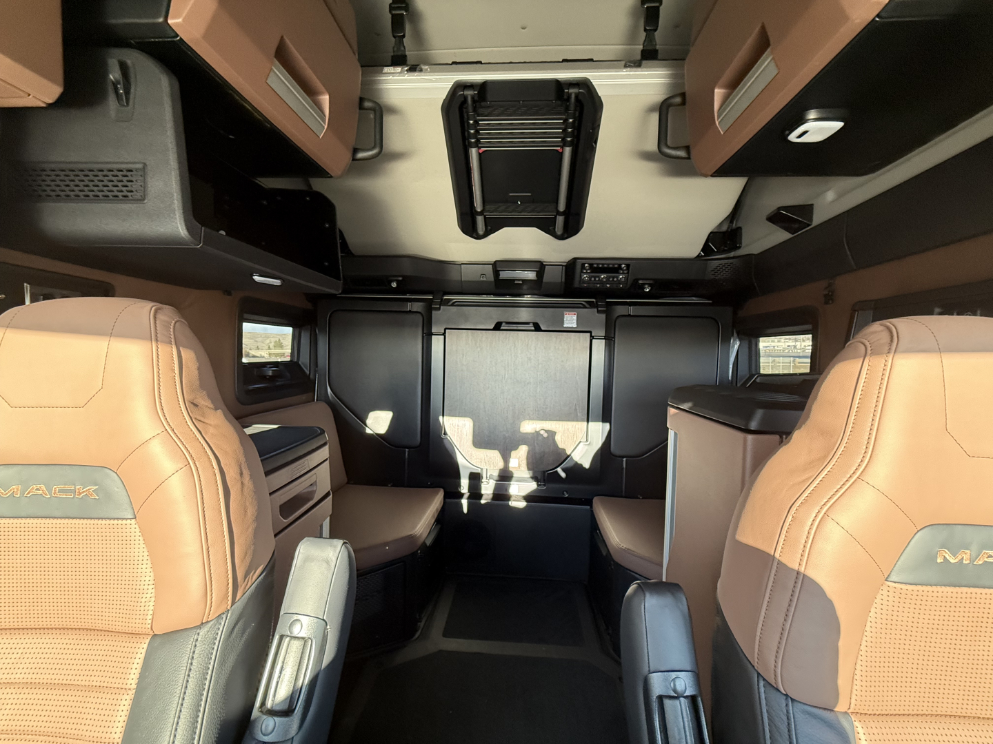 Mack PR64T76H cab interior showing tan leather seats and overhead storage, front bunk area with door and dashboard visible.
