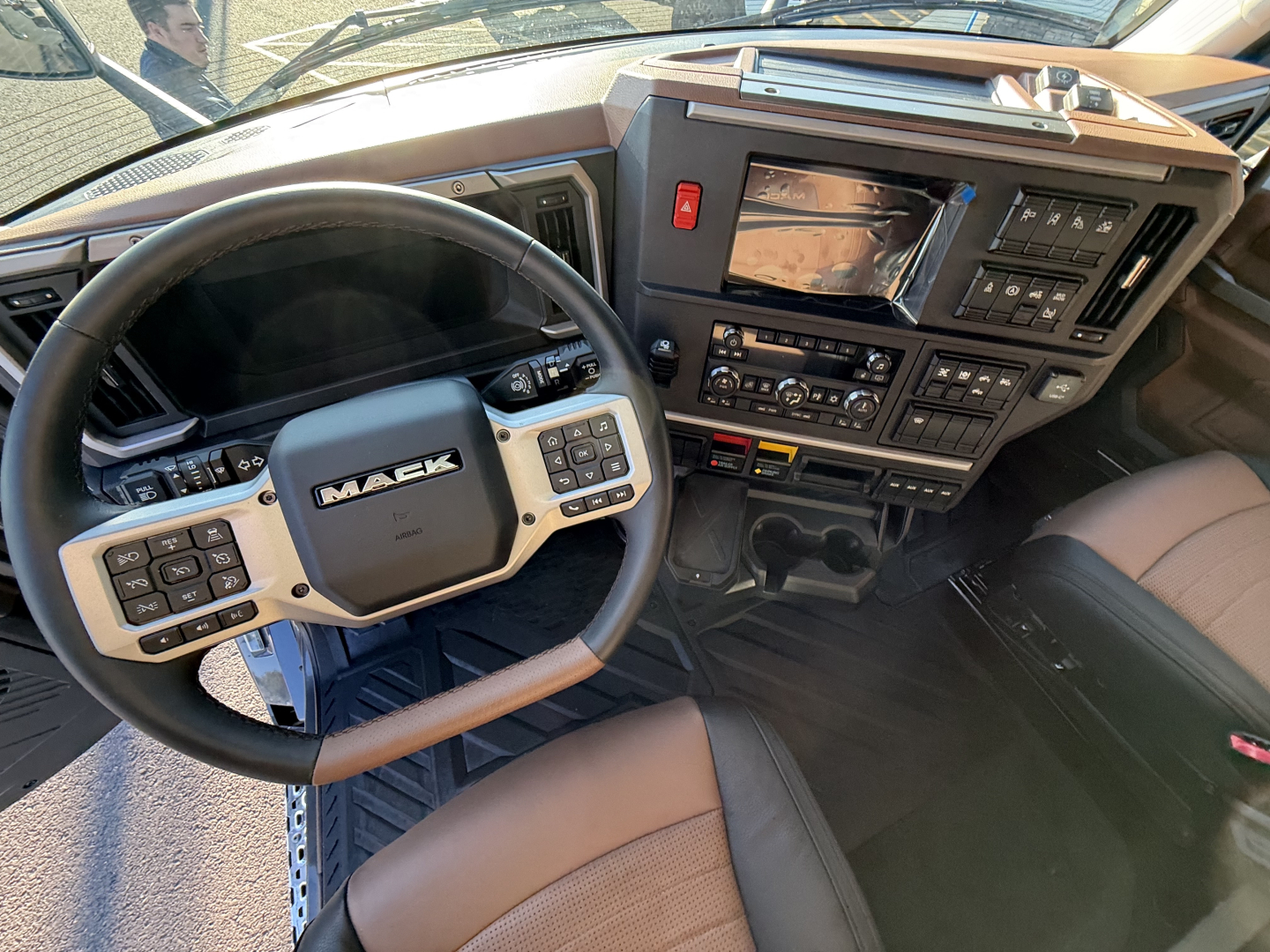 Mack PR64T76H truck interior showing steering wheel, instrument panel, and center console with numerous controls and display screens.