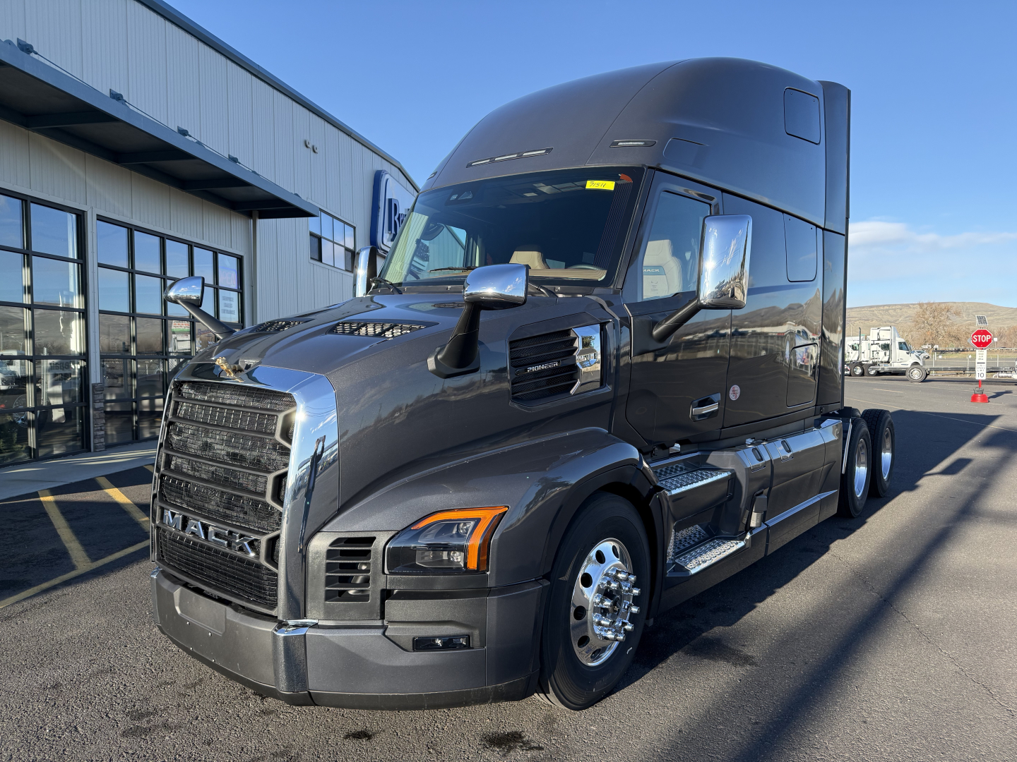 Mack PR64T76H tractor-trailer cab in view, front-left side, with chrome grille and side mirrors, parked near a dealership.