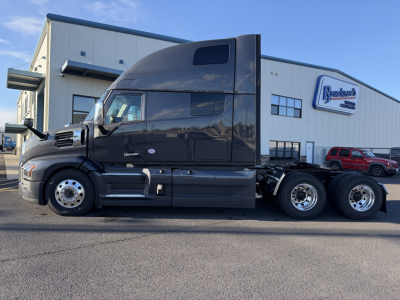 Truck side view of a black 2026 Mack PR64T76H conventional sleeper tractor, parked in front of a dealership building with a Brock’s logo sign. Visible text includes Mack, PR64T76H on listing, and wheel area.