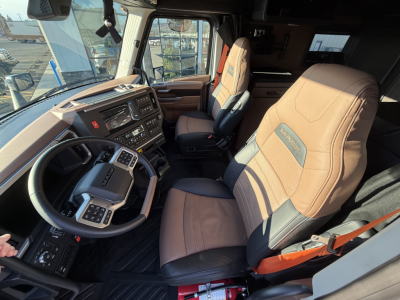 Cab interior of a 2026 Mack PR64T76H truck showing steering wheel, driver seat, and dashboard with beige and brown seats.